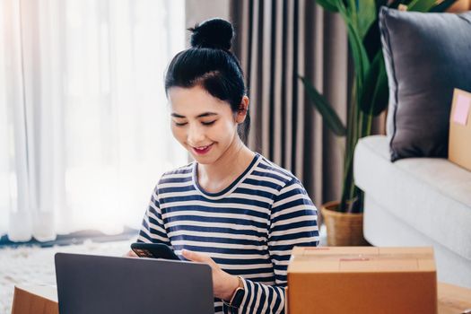 Online merchandising business idea, beautiful girl using mobile phone to see customer orders and use computer labtop to put Track And Trace parcel numbers for customers