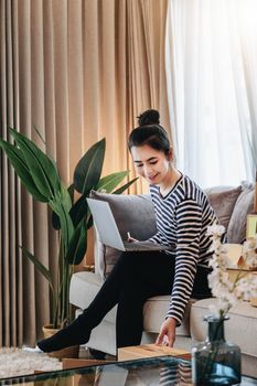 Online merchandising business idea, a beautiful girl is using a computer to check orders to deliver parcels to customers according to orders received from customers