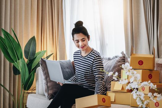 Online merchandising business idea, a beautiful girl is using a computer to check orders to deliver parcels to customers according to orders received from customers