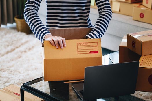 Online merchandising business idea, a beautiful girl is packing the products in the parcel delivery box to prepare the delivery to the customer according to the order received from the customer