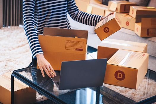 Online merchandising business idea, a beautiful girl is packing the products in the parcel delivery box to prepare the delivery to the customer according to the order received from the customer