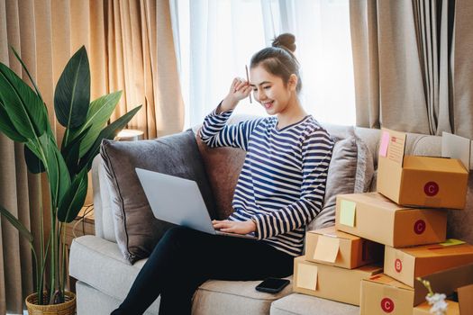 Online merchandising business idea, a beautiful girl is using a computer to check orders to deliver parcels to customers according to orders received from customers