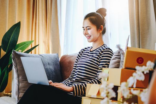 Online merchandising business idea, a beautiful girl is using a computer to check orders to deliver parcels to customers according to orders received from customers