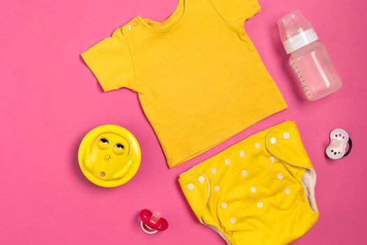 Yellow children's costume, bottle and orthodontic pacifier on a pink background. Top view. Copy space. Flat lay. Still life