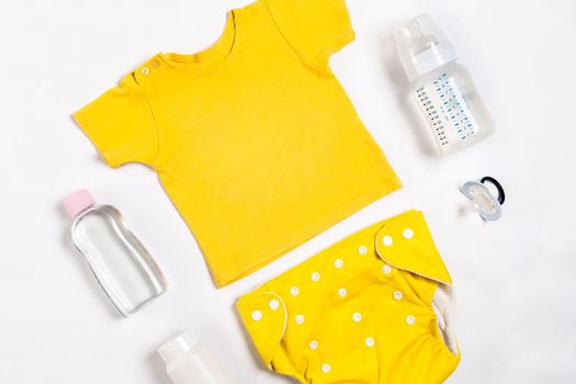 Yellow children's costume, bottle and orthodontic pacifier on a white background. Top view. Copy space. Flat lay. Still life