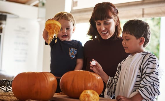 Shot of two adorable little boys carving out pumpkins and celebrating halloween with their mother at home.