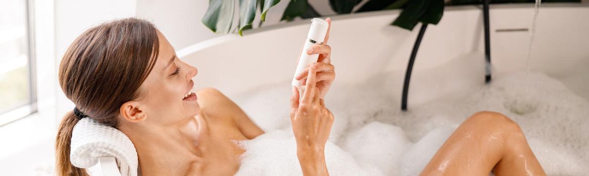 Happy young woman smiling while taking bubble bath and taking care of her skin at luxury spa resort. Wellness concept