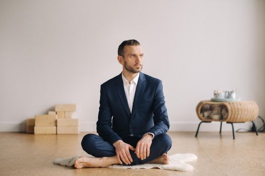 A man in a strict suit does Yoga while sitting in a fitness room.