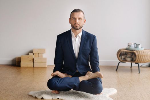 A man in a strict suit does Yoga while sitting in a fitness room.