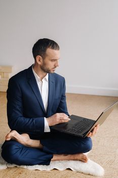 A man in a formal suit works sitting in a fitness room on a laptop.
