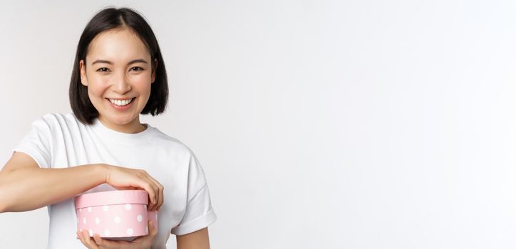 Happy asian woman, girlfriend open box with valentines day gift, receive romantic present, standing over white background. copy space