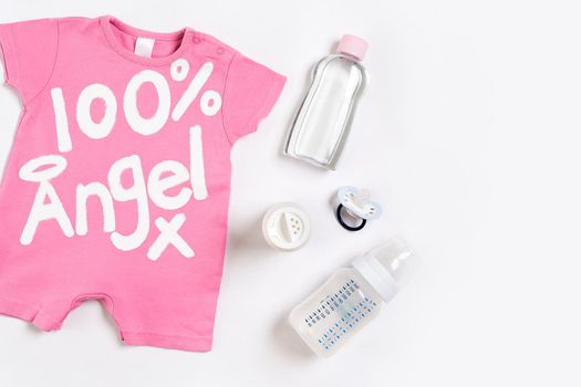 Pink children's costume, bottle and orthodontic pacifier on a white background. Top view. Copy space. Flat lay. Still life