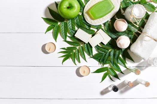 Spa set with towel and soap on white wooden background with green leaves. Top view. Copy space. Still life. Mock-up. Flat lay