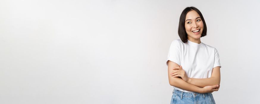 Portrait of happy asian woman smiling, posing confident, cross arms on chest, standing against studio background.