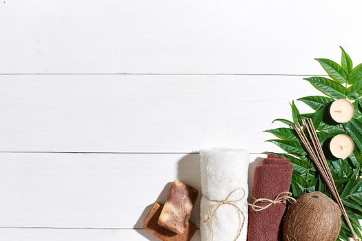 Spa set with towel and soap on white wooden background with green leaves. Top view. Copy space. Still life. Mock-up. Flat lay