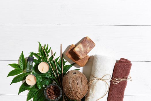 Spa set with towel and soap on white wooden background with green leaves. Top view. Copy space. Still life. Mock-up. Flat lay