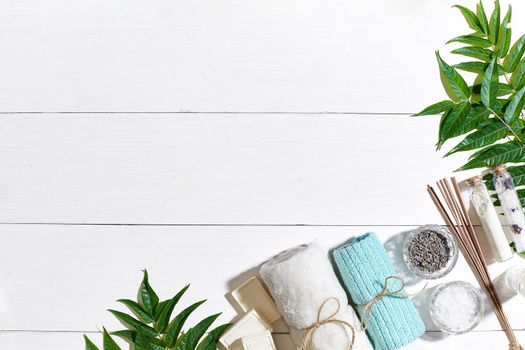 Spa set with towel and soap on white wooden background with green leaves. Top view. Copy space. Still life. Mock-up. Flat lay