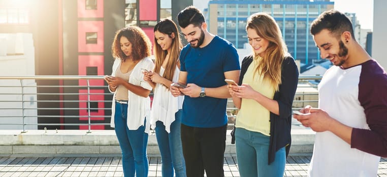Cropped shot of a group of young people texting on their cellphones while standing outdoors.