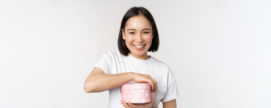 Happy asian woman, girlfriend open box with valentines day gift, receive romantic present, standing over white background. copy space