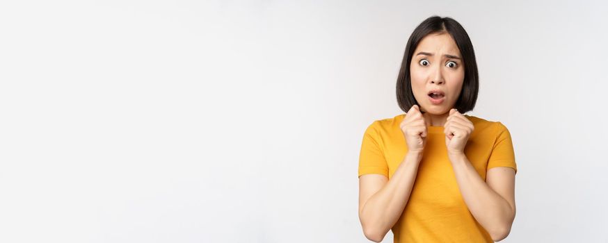 Portrait of scared asian woman shaking from fear, looking terrified and concerned, standing anxious against white background.