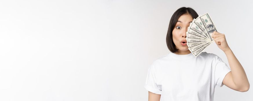 Happy asian girl holding money, cash near face, concept of microcredit and finance, white studio background. Copy space