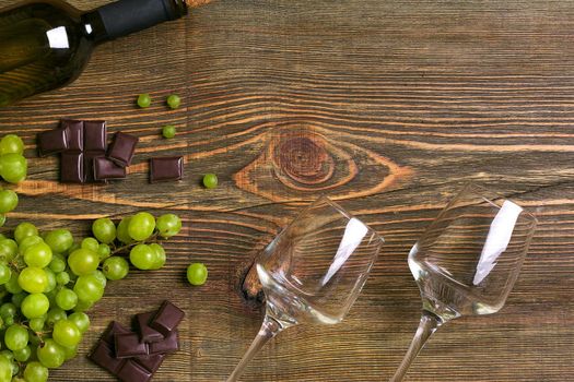 Two glasses, bottle of white wine and grape on a wooden table. Top view. Copy space. Flat lay. Still life