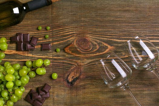 Two glasses, bottle of white wine and grape on a wooden table. Top view. Copy space. Flat lay. Still life