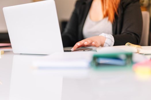 Young, red-haired business girl working on a chart in the office or at home while searching for information on the computer. The girl is wearing jeans and a black blazer.