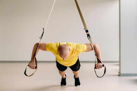 A focused male athlete performing an exercise on functional loops in the gym.