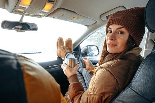 Beautiful young woman wearing warm clothes sitting in car while winter road trip, close up