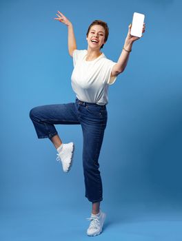 Happy woman shows blank smartphone screen against blue background, close up