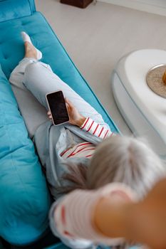 Top view of female person lying on comfortable sofa and holding modern smartphone