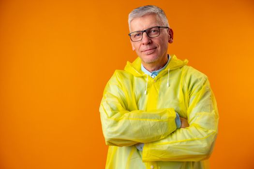 Mature man wearing raincoat over yellow background, portrait