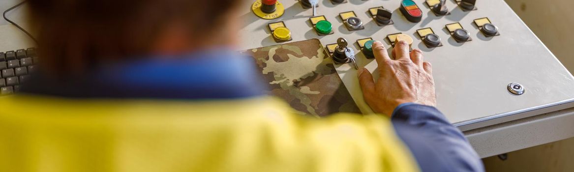 Close up of man factory worker using control panel while sitting at work desk with knobs and switches