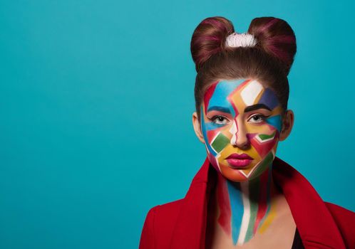 Portrait of funky girl with creative and colorful make up on face. Beautiful model wearing in red clothes, looking at camera, posing in studio. Woman has hairstyle bow, pink, plump lips.