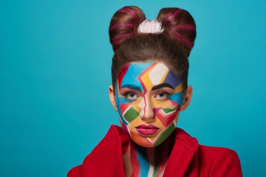 Fashion model looks like comic character, has creative, colorful pop art make up and pink plump lips. Pretty confident woman looking at camera, posing. Stylish bow hairstyle.