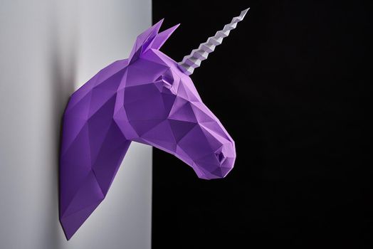 Violet unicorn's head hanging on grey shadowed wall. Object having straight lines, geometrical shape. Innovative interior design details. Made of paper. Saturated, bright color. Black background.
