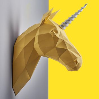 Fancy saturated yellow unicorn's head made of paper hanging on grey wall. Innovative interior design details. Straight lines. Original geometrical shape.Shadows.