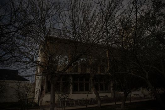 Old house with a Ghost in the forest at night or Abandoned Haunted Horror House. Old mystic building in dead tree forest. Surreal lights. Horror Halloween concept