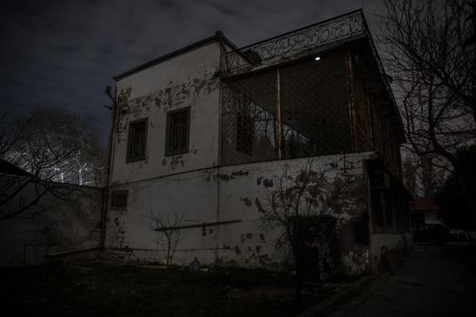 Old house with a Ghost in the forest at night or Abandoned Haunted Horror House. Old mystic building in dead tree forest. Surreal lights. Horror Halloween concept