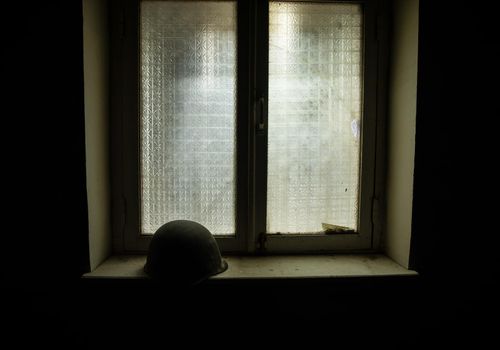 Conceptual photo of war between Russia and Ukraine. Russian helmet on windowsill at night. Old creepy room with window. Explosion outside.