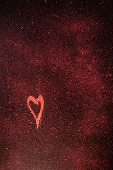 Red heart shape drawn with red chalk  on black background with red small pieces of chalk