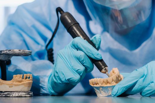 A masked and gloved dental technician works on a prosthetic tooth in his lab.