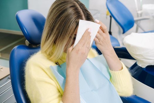 A girl wipes her face sitting in a dental office.