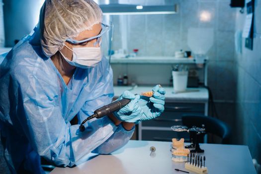 A dental technician in protective clothing is working on a prosthetic tooth in his laboratory.