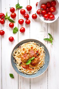 Delicious spaghetti with meatballs and tomato sauce on a plate. Serving on a white rustic wooden table. An Italian-American dish. Top view