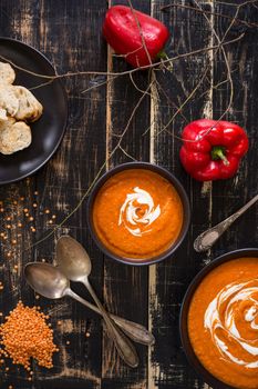 Delicious pumpkin soup with heavy cream on dark rustic wooden table with red bell pepper, bread toasts, lentil and autumn branches. Top view