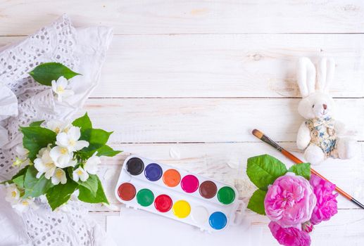 Desk of creative worker. Paints, brush and flowers. Top view background