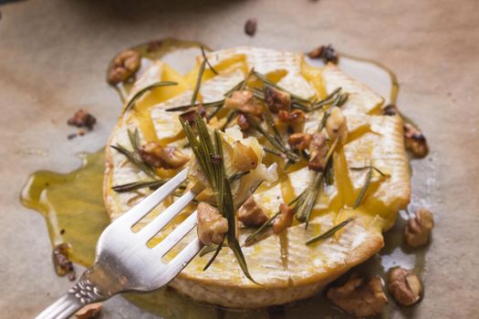 Piece of baked camambert on a fork. Delicious baked cheese with honey, walnuts, herbs and pears