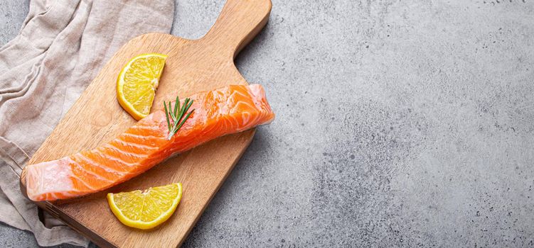 Raw salmon fish fillet with lemon wedges and rosemary on wooden cutting board on gray stone concrete rustic background kitchen table from above, healthy eating and diet, space for text